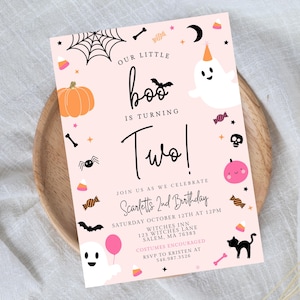 May include: A rectangular birthday invitation card with a light pink background featuring Halloween-themed illustrations including ghosts, a pumpkin, a spider, a bat, a black cat, and candy. The text reads Our Little Boo Is Turning Two!