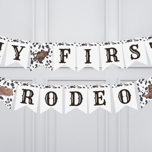 May include: White banner with black letters that read "My First Rodeo". The banner has a cowhide pattern with a brown cowboy boot, a brown cowboy hat, and a brown bull on it.