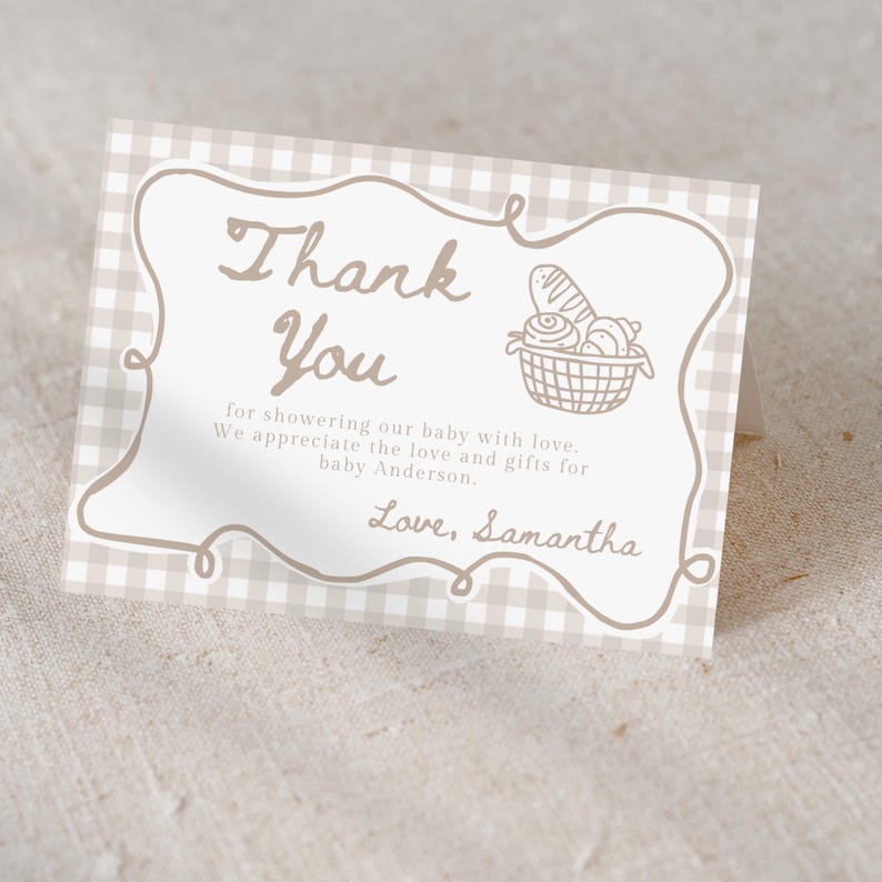 May include: A folded thank you card with a beige gingham pattern background. The card features a decorative border and the words "Thank You" in a handwritten style. A basket of bread is illustrated on the right. The text reads "for showering our baby with love...Love, Samantha."