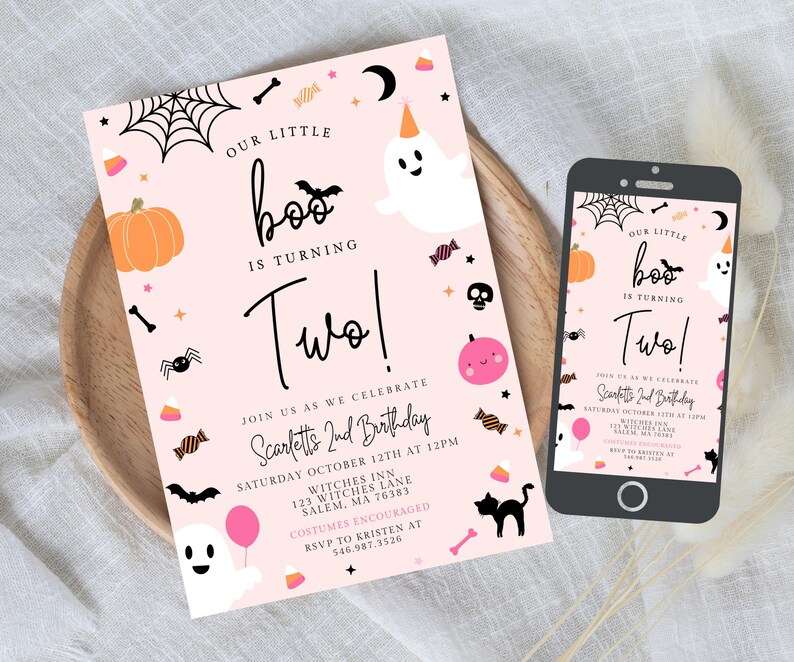 May include: A light pink birthday invitation card and a smartphone displaying the same design. The card features a white ghost, an orange pumpkin, a black spider, a black cat, and text reading Our Little Boo Is Turning Two, Scarlett's 2nd Birthday.