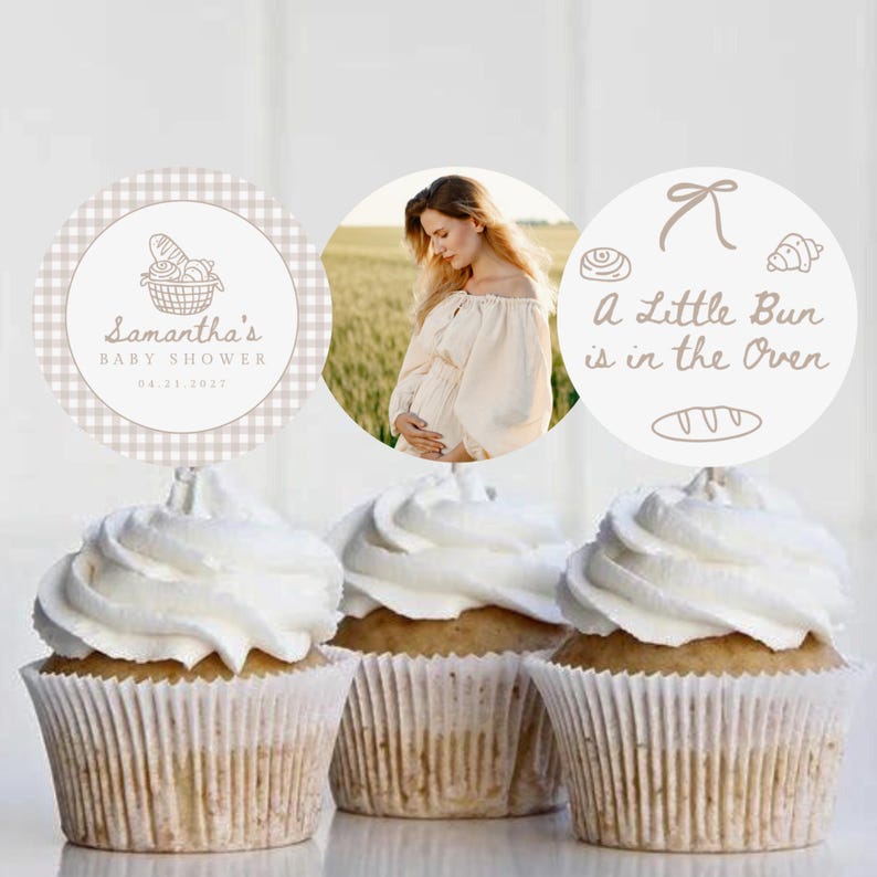 May include: Three cupcakes with white frosting and decorative toppers. One topper has a photo of a pregnant person, another says "A Little Bun is in the Oven", and the last says "Samantha's Baby Shower".