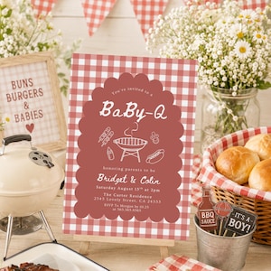 May include: A baby shower invitation with a red and white gingham pattern, featuring the text "BaBy-Q". The invitation is on a small easel, with a miniature grill, flowers, and a basket of rolls in the background. The invitation text reads "Buns, Burgers & Babies".