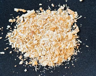May include: A pile of light brown, chopped, and shredded pieces of what appears to be dried plant material. The pieces vary in size and shape, with some appearing like small sticks and others like flakes. The background is a solid black.