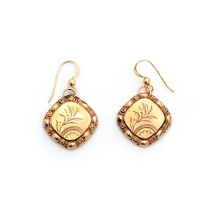 May include: A pair of gold-toned earrings with a square-shaped design featuring a floral pattern. The earrings have a delicate, intricate design.