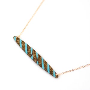 Puede incluir: Un collar de cadena dorada con un colgante largo y delgado. El colgante est&aacute; hecho de lat&oacute;n y tiene un patr&oacute;n de espiral con rayas azules.