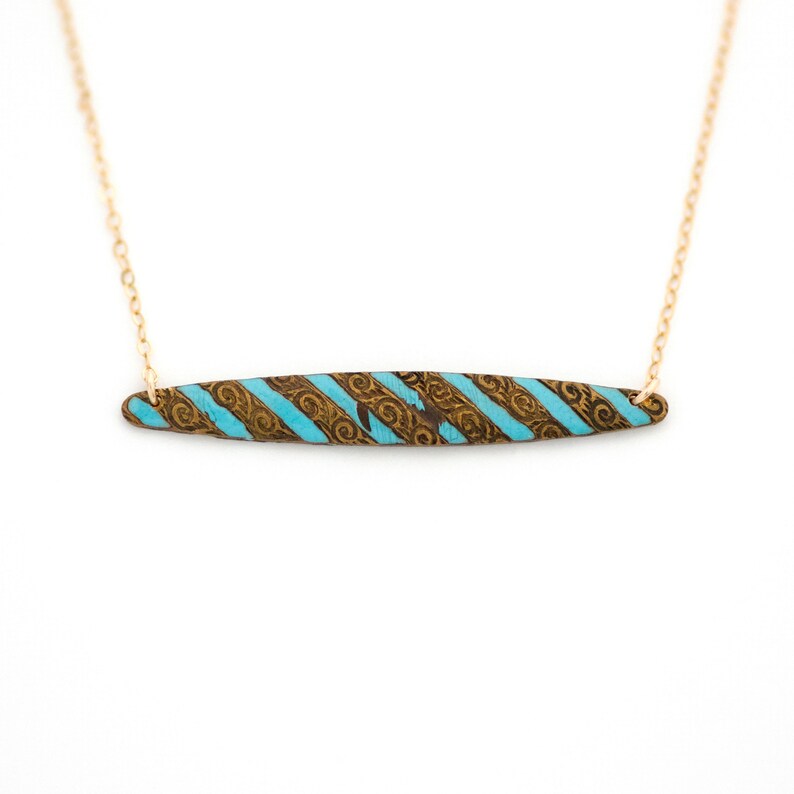 Puede incluir: Un collar de cadena dorada con un colgante de barra turquesa y dorada. La barra tiene un patr&oacute;n de rayas y un dise&ntilde;o intrincado.