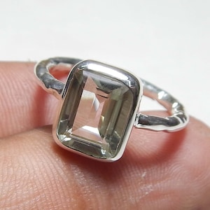Könnte beinhalten: Ein Silberring mit einem rechteckigen, hellgrünen Edelstein. Das Band des Rings hat ein strukturiertes, gehämmertes Aussehen. Der Edelstein ist in einer Lünettenfassung gefasst. Der Ring ist ein Schmuckstück.