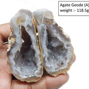 May include: A geode with a white and grey interior and a brown exterior. The geode is split in half and the two halves are held together by a hand. The geode weighs 118.5 grams. Agate Geode (A) weight: - 118.5gm