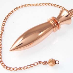 Op de afbeelding: Een koperkleurige pendel met een puntig uiteinde en een decoratieve bovenkant. De pendel is bevestigd aan een ketting, en de ketting eindigt met een kleine, ronde kraal. Het object is ontworpen voor waarzeggerij en spirituele praktijken.