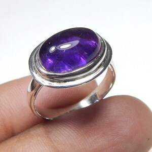 May include: A silver ring featuring a large, oval amethyst gemstone. The ring has a double band design with a smooth, polished finish.