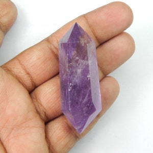 May include: A faceted amethyst crystal point, showcasing a deep purple hue. The crystal is held in a hand, highlighting its polished surfaces and geometric shape. This gemstone is a natural, decorative item.