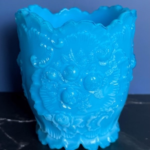May include: A vintage blue glass vase with an ornate floral design. The vase has a scalloped rim and a wide base.