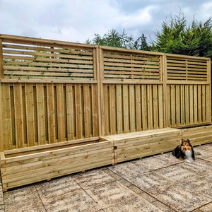 May include: A wooden garden fence with slatted panels and three built-in planter boxes. The fence is made of natural wood and has a rustic look. A small dog is sitting in front of the fence.