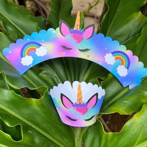 Op de afbeelding: Twee cupcake-verpakkingen met een eenhoornontwerp met een regenboog en sterren. De verpakkingen zijn blauw, paars en roze met een witte achtergrond.