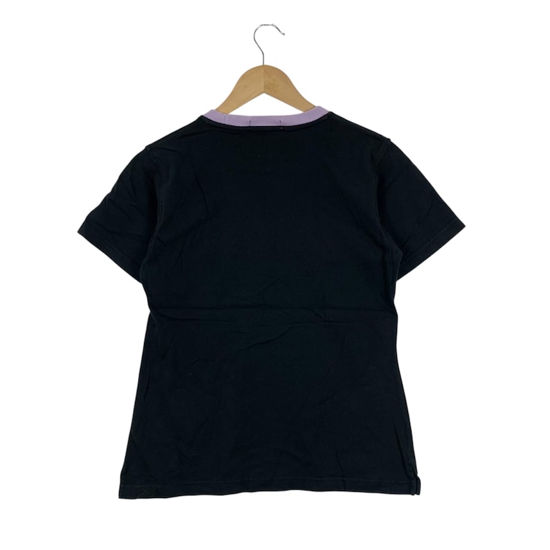 May include: Black t-shirt with a purple collar, hanging on a wooden hanger. The short-sleeved shirt is made of a soft material. The back of the shirt is visible, showing the collar and the shape of the garment.