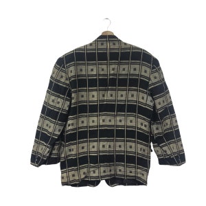 May include: A black and tan plaid blazer hanging on a wooden hanger. The blazer has a square pattern design. The blazer has two front pockets and three buttons on each sleeve. The blazer is made of a woven fabric.