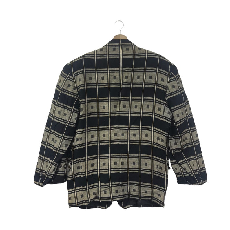 May include: A black and tan plaid blazer hanging on a wooden hanger. The blazer has a square pattern design. The blazer has two front pockets and three buttons on each sleeve. The blazer is made of a woven fabric.