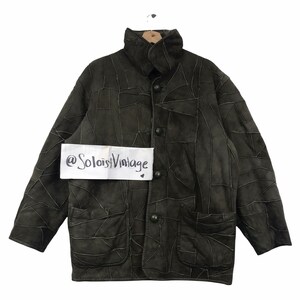 Puede incluir: Chaqueta patchwork verde oliva oscuro con cuello alto y cierre de botones. La chaqueta presenta dos bolsillos delanteros y un diseño único, con el texto "@SoloistVintage" en una etiqueta blanca.