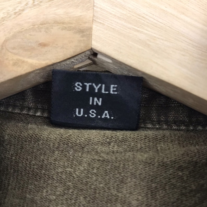 May include: A white ceramic mug with a black handle and the text "But First, Coffee" in a bold, black font. The mug is set against a blurred background, suggesting a cozy setting.