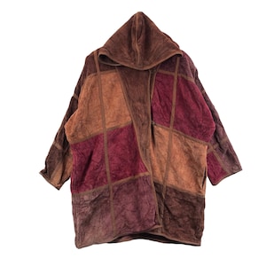 May include: A hooded patchwork coat in shades of brown, burgundy, and tan. The coat features a geometric design with square and rectangular panels. The long sleeves and hood provide extra warmth. The coat is made of a soft, textured fabric.