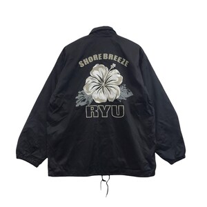 May include: Black nylon jacket with a drawstring hem. The back features a large floral design with the text "SHORE BREEZE" above and "RYU" below the flower. The flower is white and gray, with gray leaves.