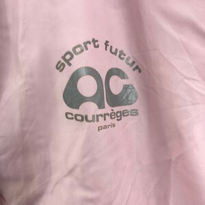 May include: A close-up of a pale pink fabric with the words "sport futur" and "courr&egrave;ges paris" printed in silver. The logo features the letters "AC" in a stylized design.