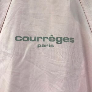 May include: Pale pink fabric with the text "courr&egrave;ges paris" printed in a muted green colour. The fabric has a slightly wrinkled texture, and the text is centred.