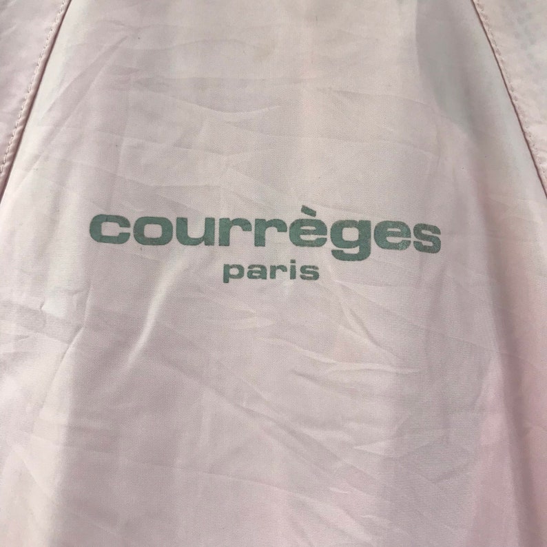 May include: Pale pink fabric with the text "courr&egrave;ges paris" printed in a muted green colour. The fabric has a slightly wrinkled texture, and the text is centred.