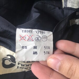 May include: Close-up of a clothing label with the text "EBDCE-12590". The label includes washing instructions and fabric composition details: 50% linen and 50% cotton. The label is attached to a black fabric.