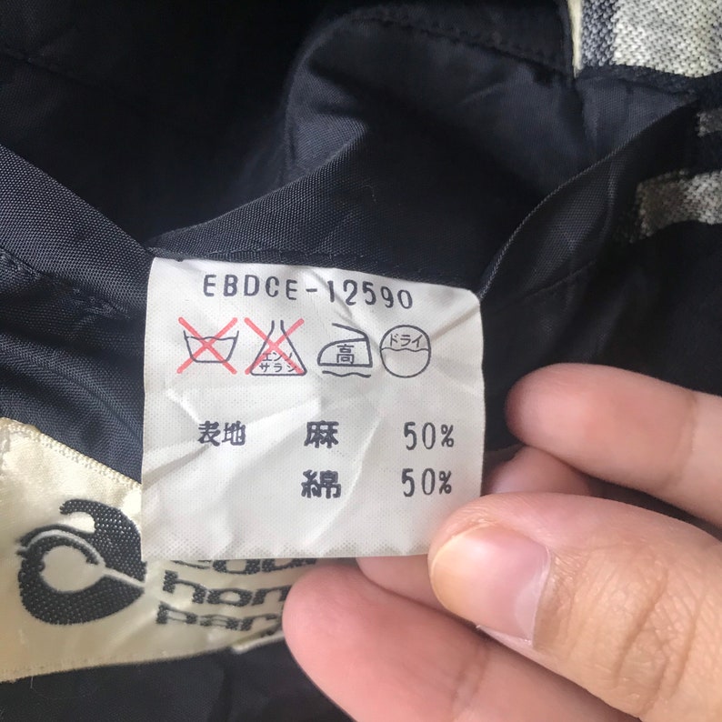 May include: Close-up of a clothing label with the text "EBDCE-12590". The label includes washing instructions and fabric composition details: 50% linen and 50% cotton. The label is attached to a black fabric.