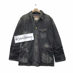 May include: A vintage black denim jacket with a collared neckline, four front pockets, and gold-colored buttons. The jacket has a faded appearance and features decorative stitching on the sleeves. The label reads "Levi's". The text "@SoloisVintage" is on a white sticker.
