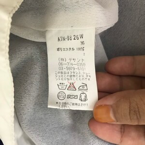 May include: A white tag with black text and symbols. The tag includes the text "ATN-88 26 W", "36", and "ポリエステル 100%", along with washing instructions and the company name. The tag is attached to a white and blue garment.