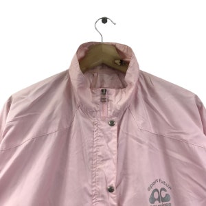 May include: A pale pink jacket with a high collar and a silver zip. The jacket features two silver press studs and the words "sport futur" and "courreges" printed in grey.
