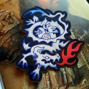 May include: A sticker featuring a stylized dragon design. The dragon is white with blue accents and outlined in black. A red flame design is on the right. The sticker has the text "VINTSONI" on it.