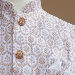 May include: White waistcoat with a gold embroidered floral pattern and gold buttons. A white pocket square is in the pocket. The text on the tag reads "KAASH COLLECT House of Indian Ethnic Wear for Women, Men & Kids www.kaashcollection.com 415-827-9482 Sarees, Suits, Readymade blouses, Dupattas, Kurta Pajamas for Mens and Boys 405 Boulder Ct, Suite 200 Pleasanton"