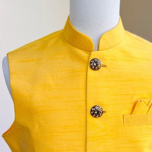 May include: A yellow sleeveless vest with a mandarin collar and five decorative buttons. The vest has a pocket on the right side with a folded yellow handkerchief.