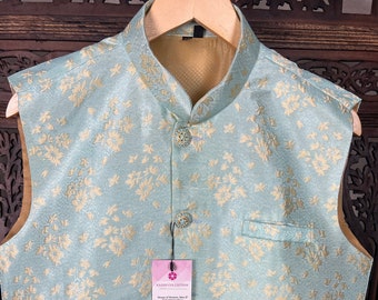 Könnte beinhalten: Eine hellblaue, ärmellose Weste mit goldfarbenem Blumenmuster und goldenen Knöpfen. Die Weste hat einen Stehkragen und zwei Taschen. Die Weste hat ein Etikett mit der Aufschrift "Kashi Collection, House of Silks, Made in India, www.kashicollection.com, Pasadena, California, 415-677-9682, come visit us! come get fit!"