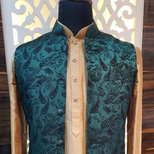 May include: A teal waistcoat with a paisley pattern and black buttons. The waistcoat is worn over a gold kurta.