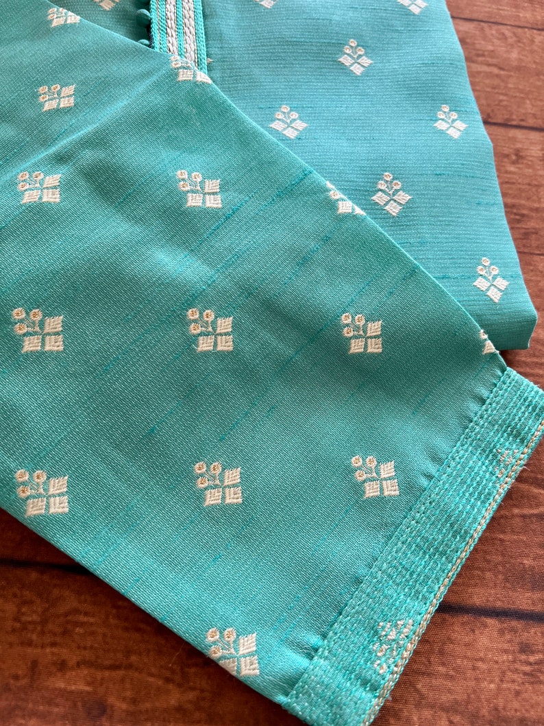 Pode incluir: Um tecido azul turquesa com um padr&atilde;o floral branco. O tecido tem uma guarni&ccedil;&atilde;o dourada ao redor das bordas.