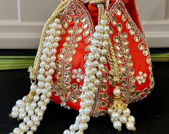 May include: A bright orange drawstring bag with gold and silver embroidery and a pearl tassel. The bag is decorated with a floral pattern and has a gold clasp.