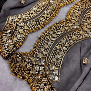May include: Close-up of black sheer fabric with gold and silver embroidery and beading. The fabric has a delicate, intricate design.