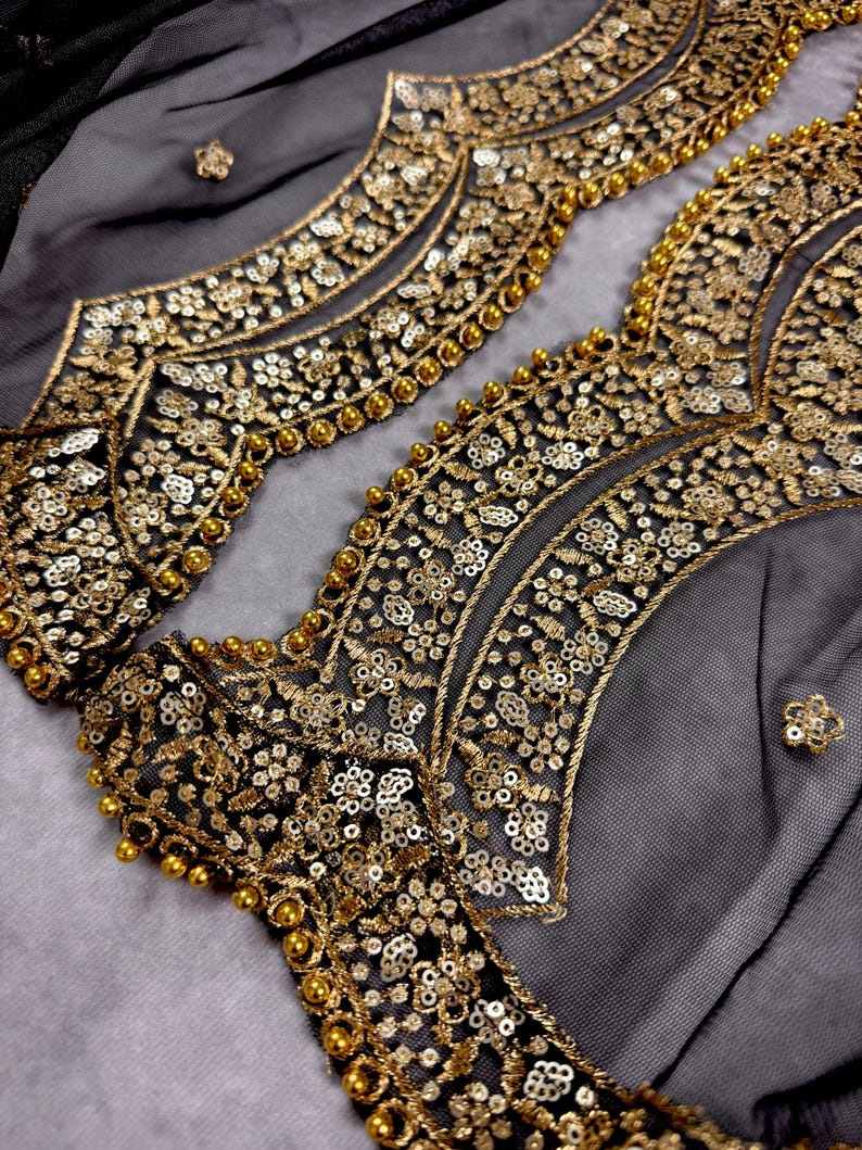 May include: Close-up of black sheer fabric with gold and silver embroidery and beading. The fabric has a delicate, intricate design.
