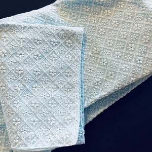 Pu&ograve; includere: Un tessuto blu chiaro con un motivo ricamato bianco di piccoli fiori a forma di diamante.