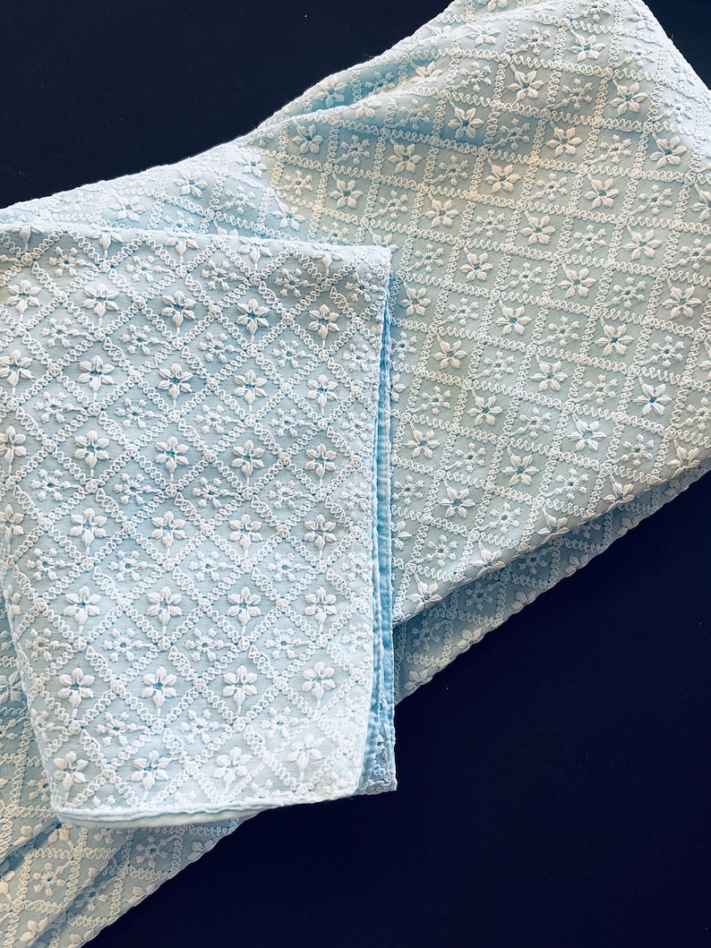 Pu&ograve; includere: Un tessuto blu chiaro con un motivo ricamato bianco di piccoli fiori a forma di diamante.