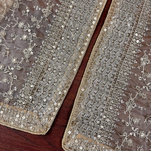May include: Close-up of two sections of a sheer, beige fabric, heavily embellished with silver sequins and floral embroidery. The edges are trimmed with a border of sequins. The fabric is likely used for formal wear or decorative purposes.