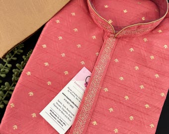 May include: A pink kurta with gold embroidery and trim. The kurta has a mandarin collar and a button closure. The fabric is a lightweight silk blend. The tag on the kurta reads "Kaash Collection, House of Indian Ethnic Wear for Women, Men & Kids, www.kaashcollection.com, 415-827-9482, Sarees, Suits, Readymade Blouses, Dupattas, Kurta Pajamas for Mens and Boys, 405 Boulder Ct, Suite 200-4, Pleasanton, California."