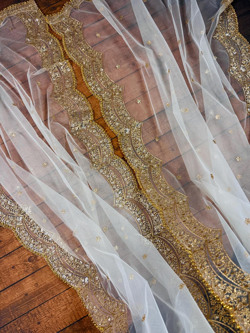 May include: White sheer fabric with a gold beaded trim. The trim features a scalloped design with a repeating pattern of small gold beads and sequins.