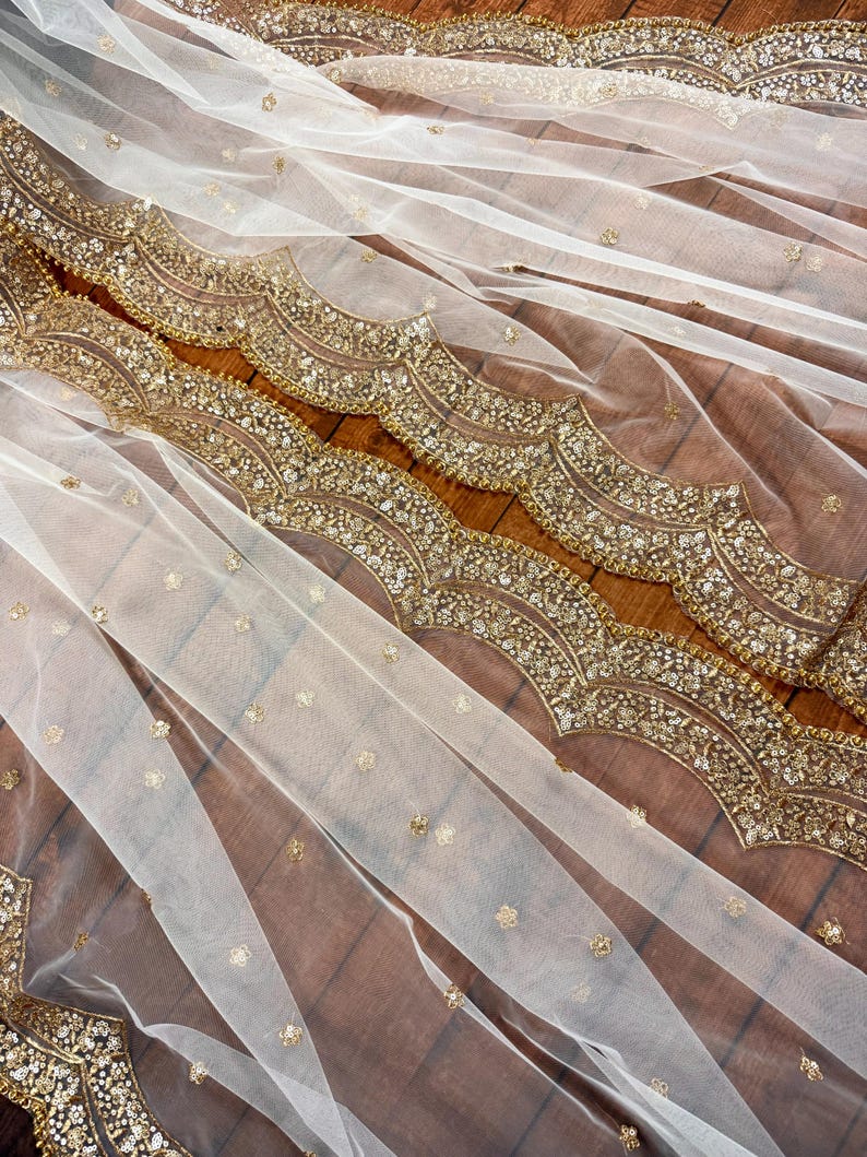 May include: White sheer fabric with a gold beaded trim. The trim features a scalloped design and is embellished with sequins.