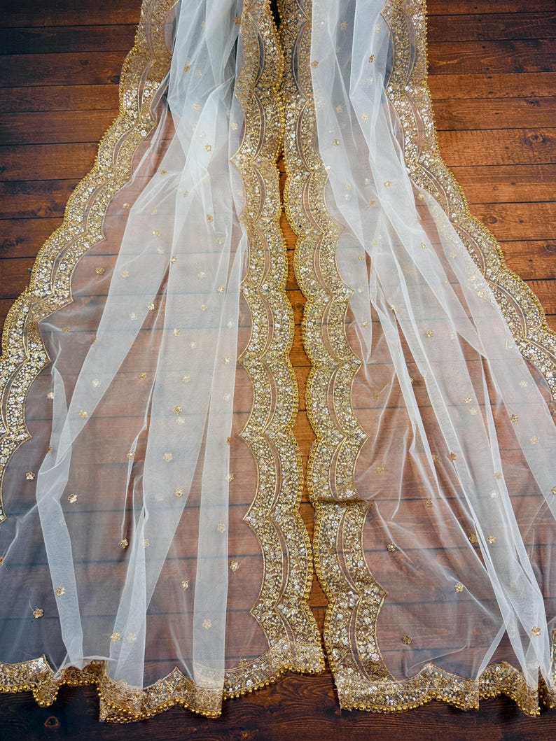 May include: White sheer fabric with a gold beaded trim. The trim features a scalloped edge and is decorated with sequins.