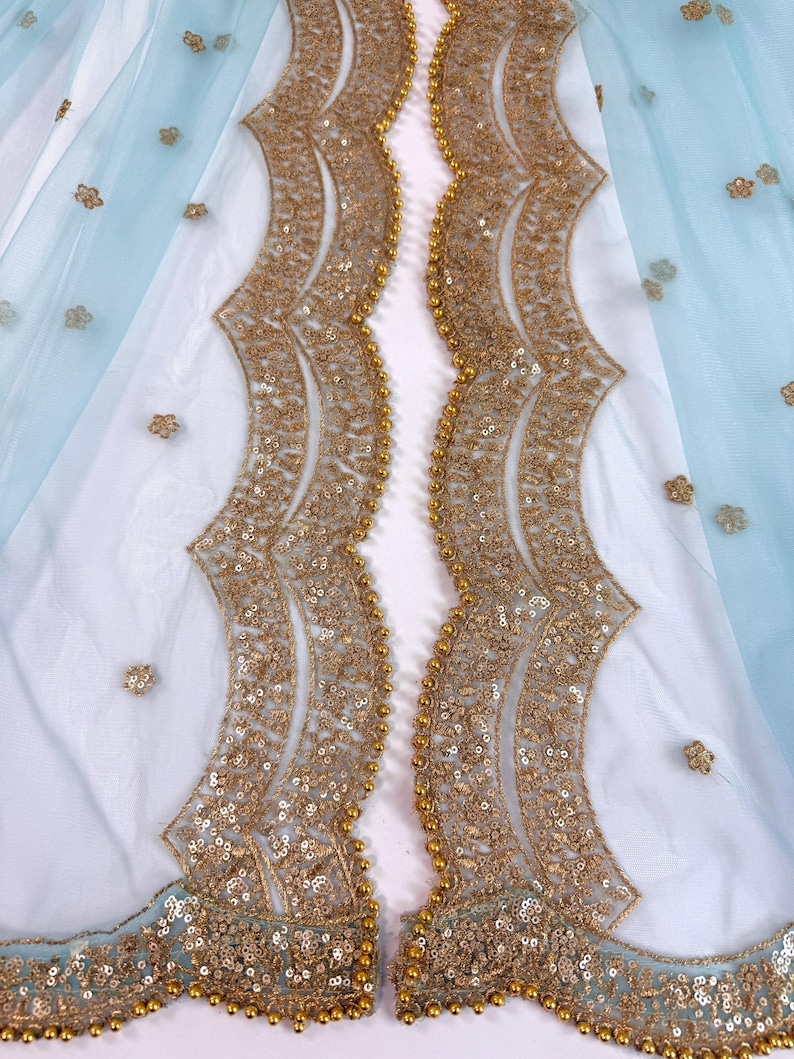 May include: A delicate light blue fabric with gold embroidery. The design includes scalloped edges and is adorned with gold sequins and small floral details. The fabric is layered over a white material, creating a layered effect.